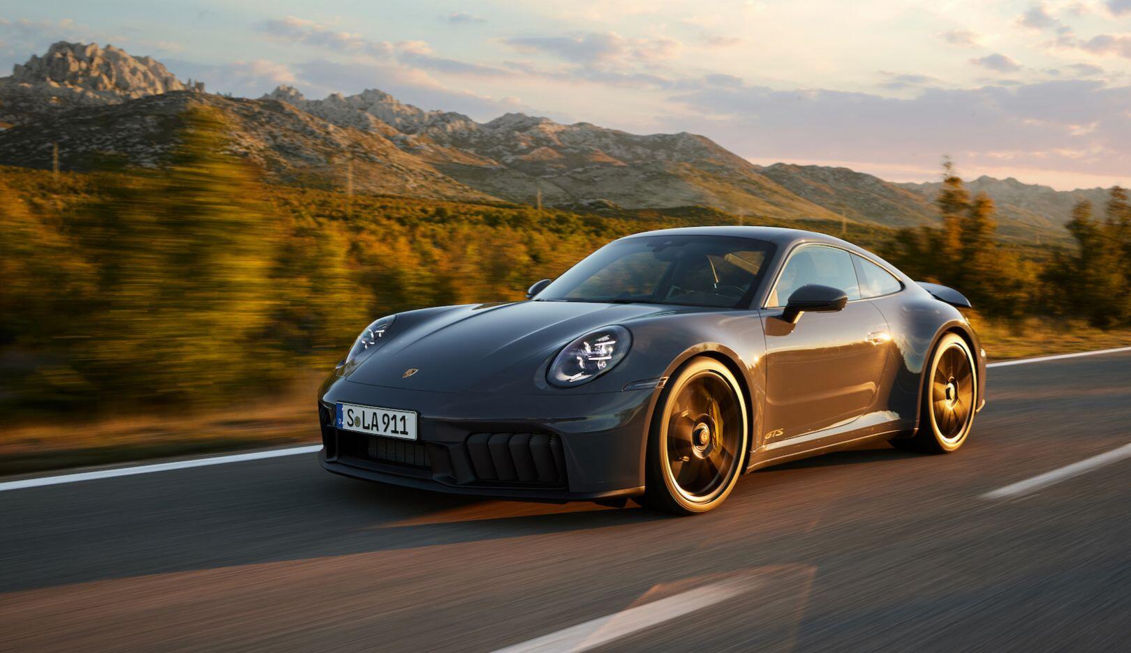 A black sports car driving to the left along a road, mountains in the background