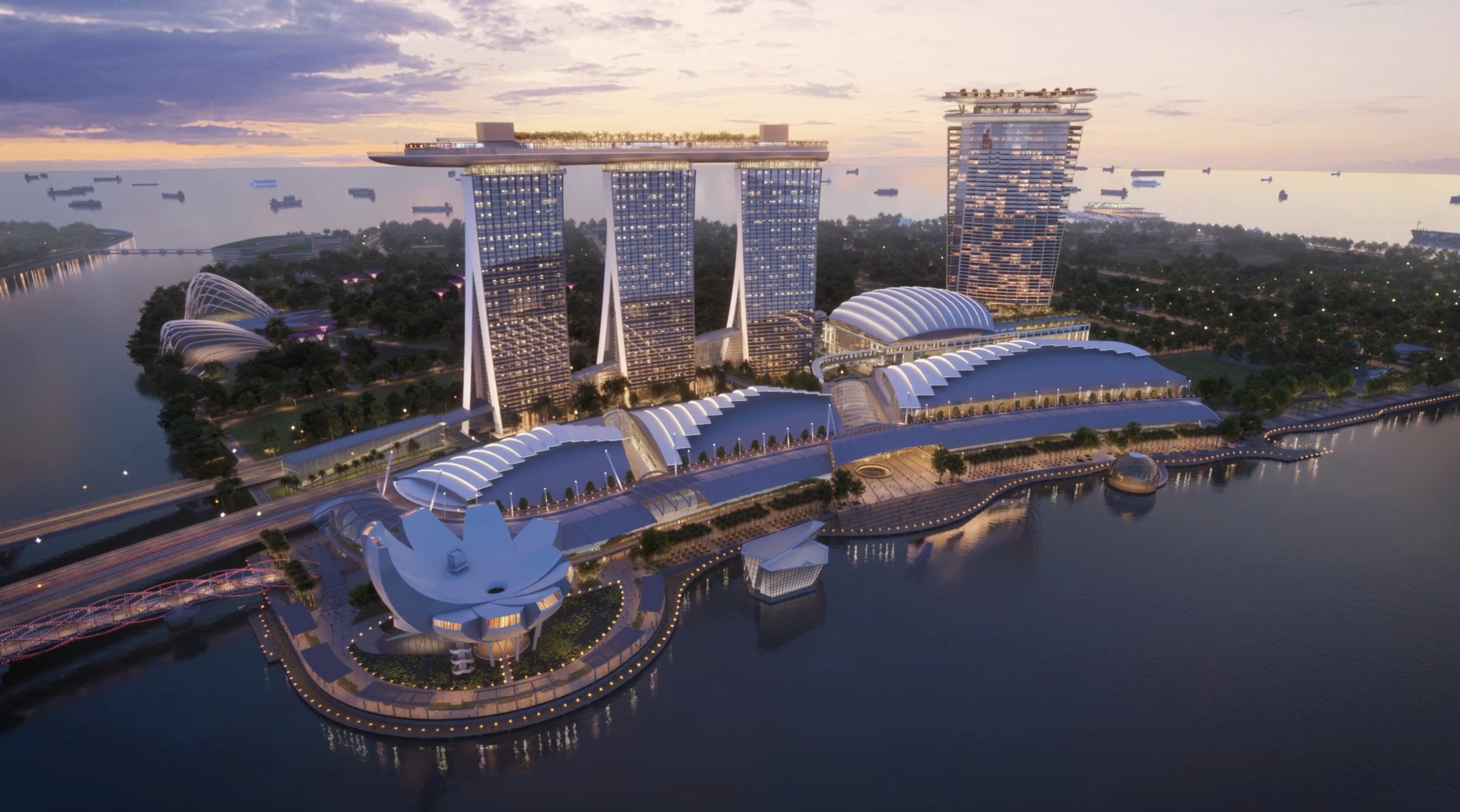 An oval tower to the right of Marina Bay Sands' three towers, with more precincts below and Marina Bay in the foreground