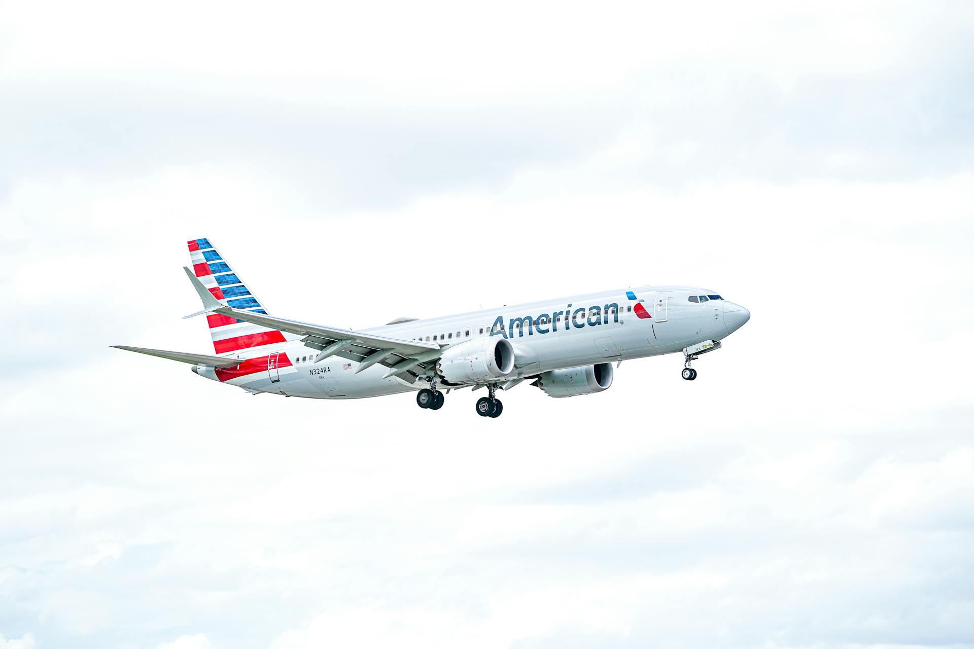 An American Airlines-branded plane flying, white with red and blue stripes on the tail
