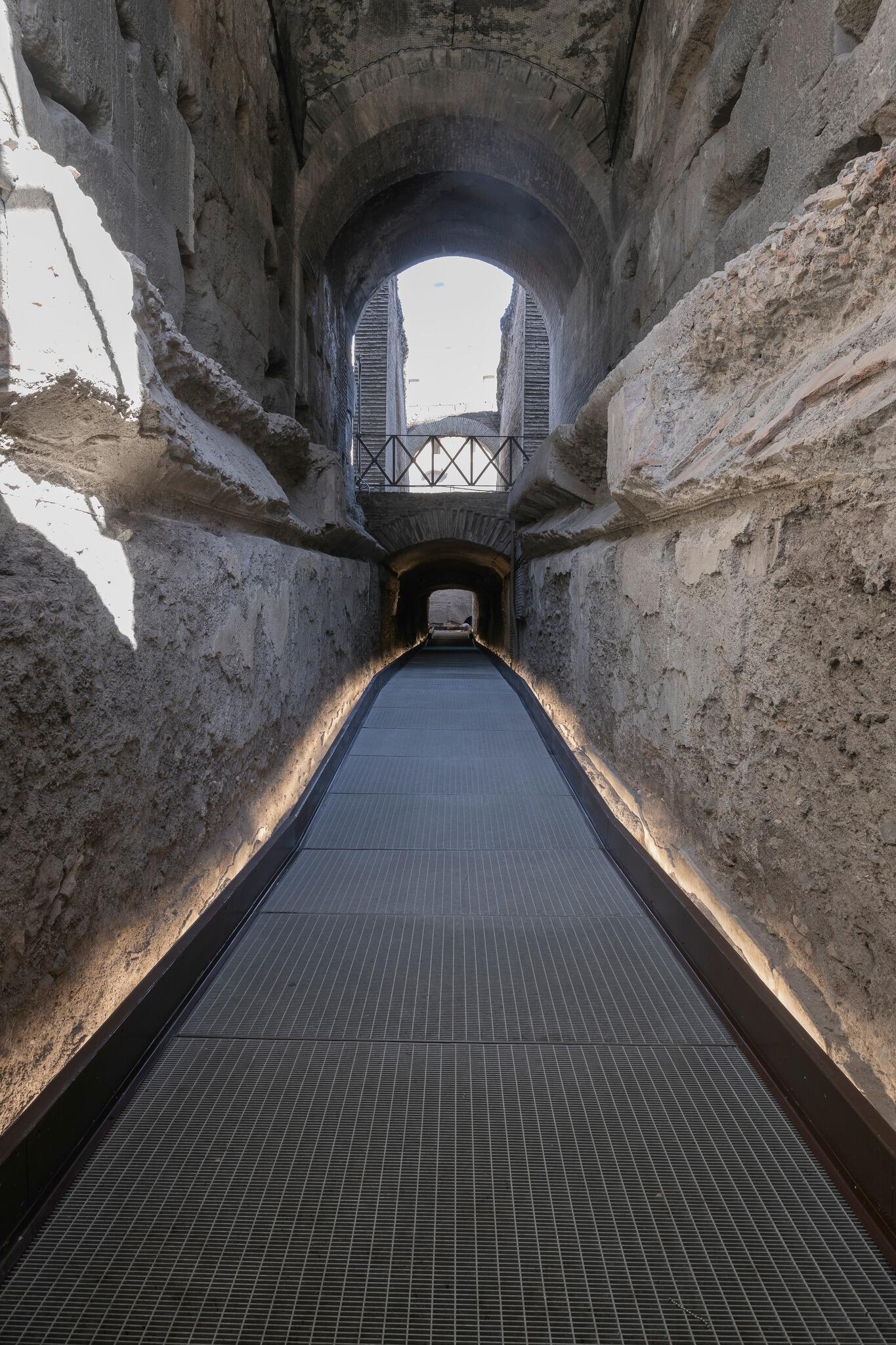 A lit walkway through a stone passage, with another passage and the ground level seen above