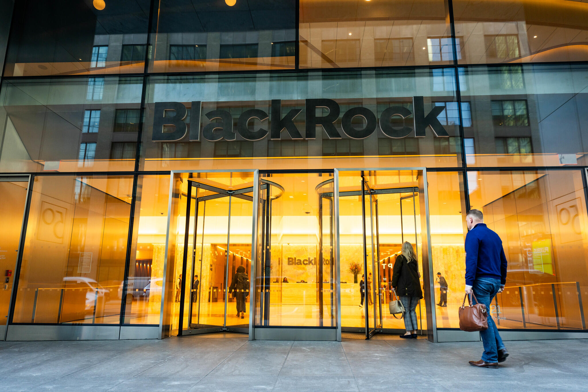 Two people standing in front of rotating glass doors below a sign reading "BlackRock"