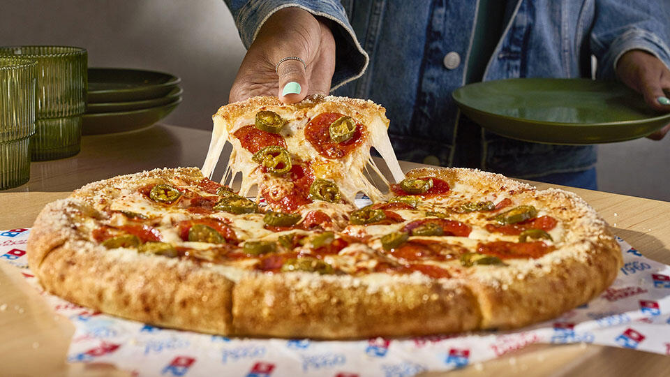 A hand pulling a slice of pizza with a cheese-stuffed crust from the rest of the pizza