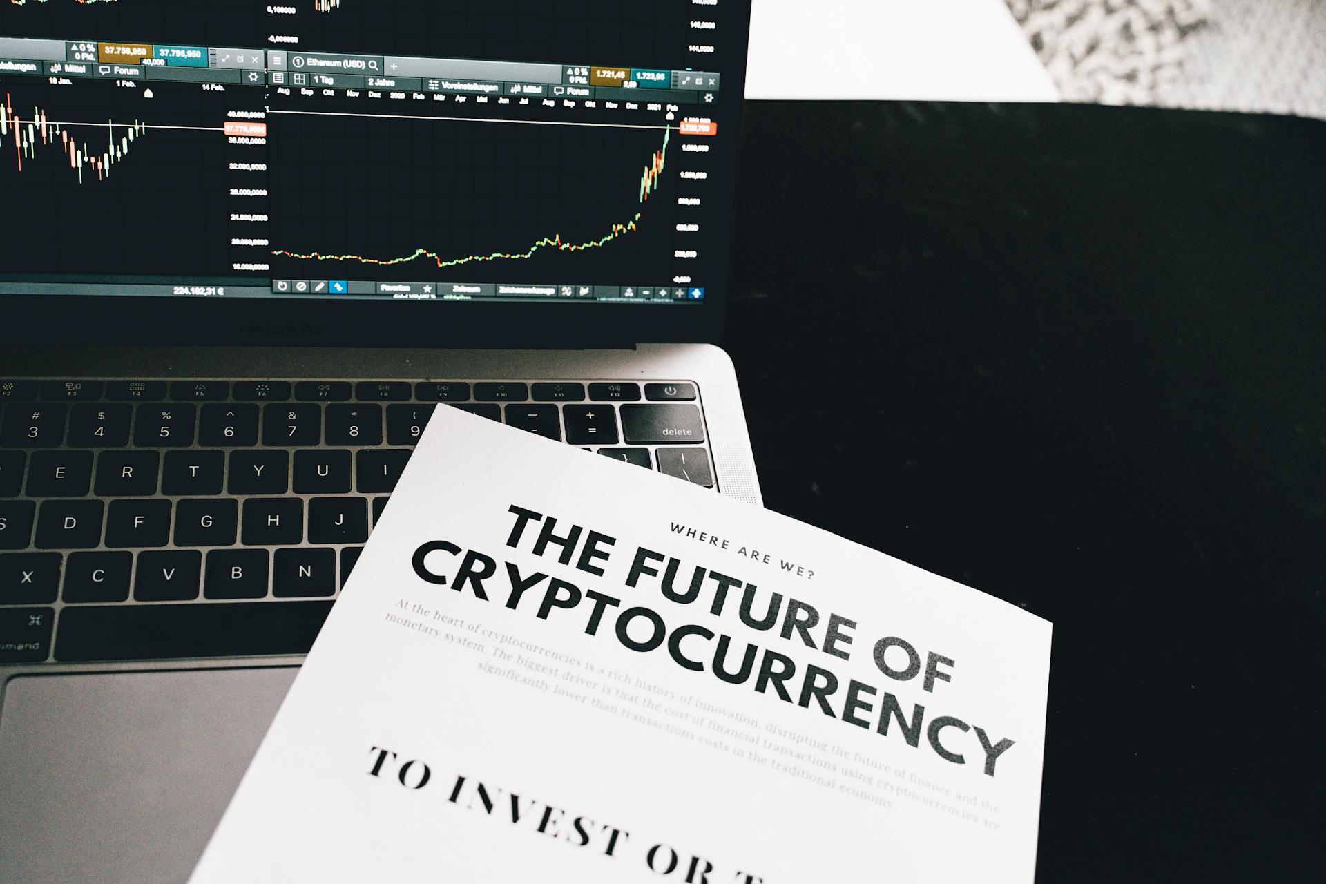 Paper reading "Where Are We? The Future of Cryptocurrency" over a laptop showing Bitcoin data