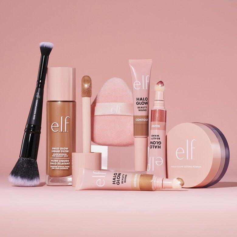 An e.l.f.-branded makeup brush and sponge with other liquid makeup products on a pink background