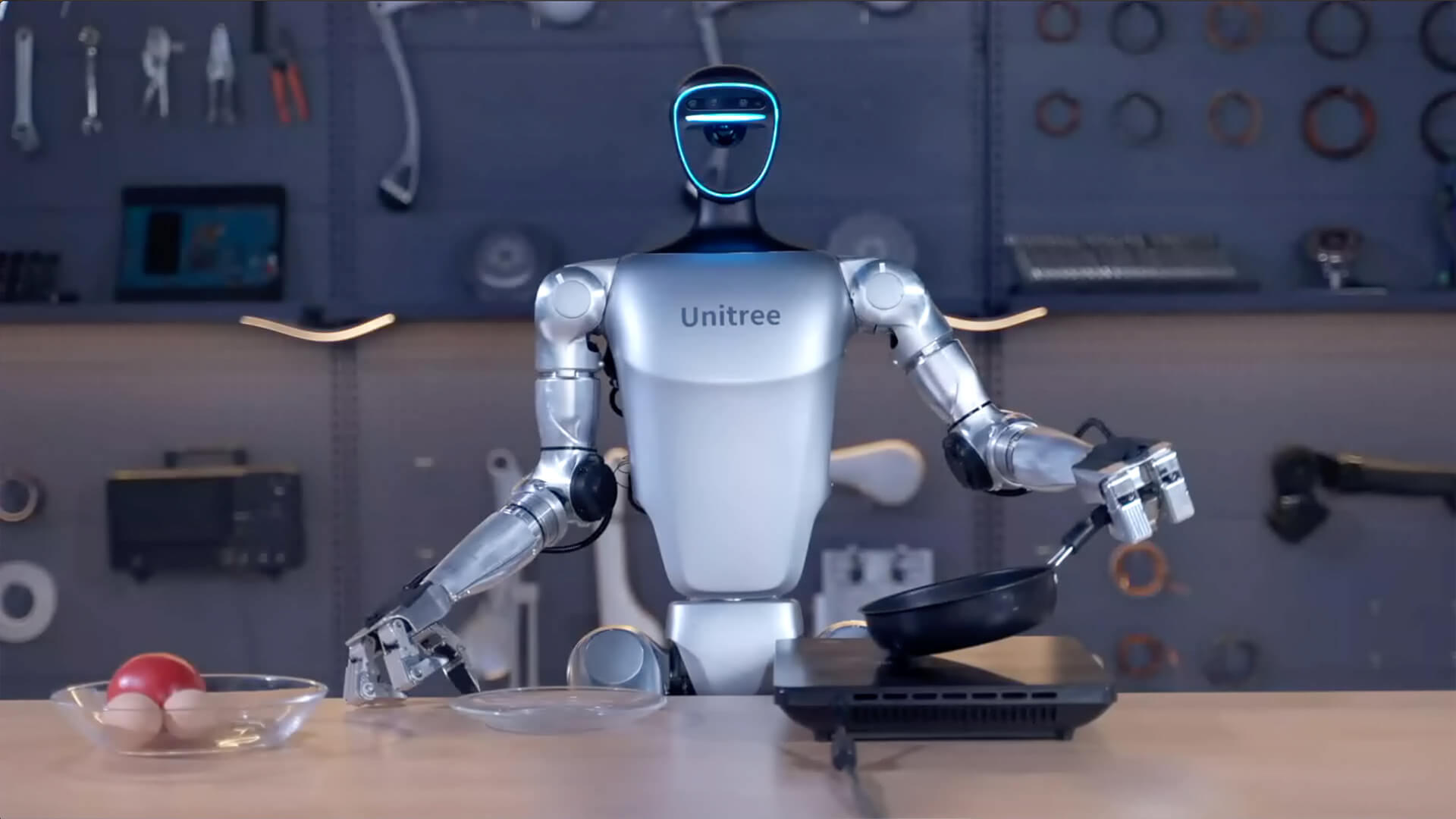 A humanoid robot holding a frying pan over a heating unit