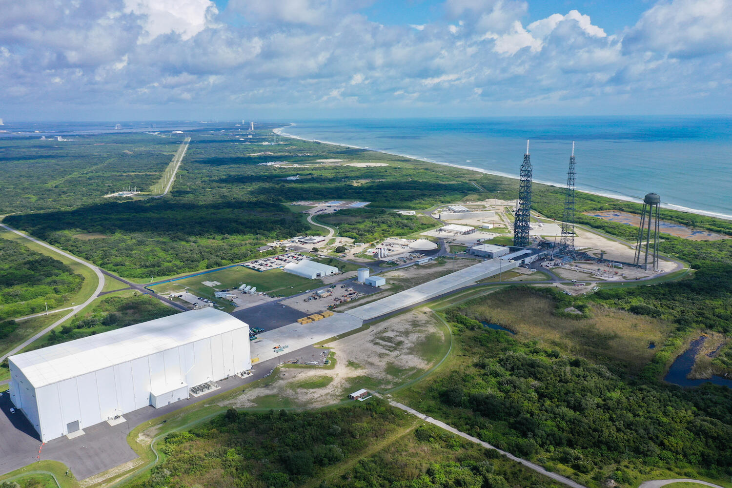 A rocket launch site with three towers, a tarmac, and a hangar.