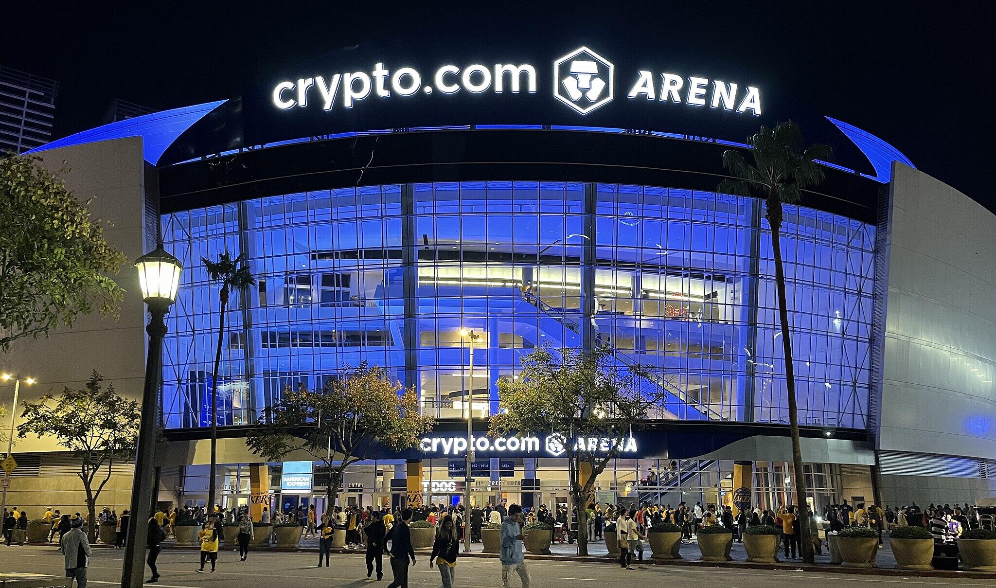 Exterior of Crypto.com Arena. People entering below a large, blue-tinted glass facade, with "crypto.com ARENA" at the top