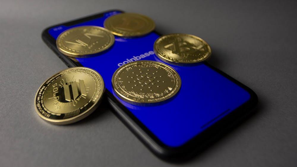 A phone displaying Coinbase's entry screen with five gold coins on top